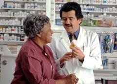 Photograph of a pharmacist with a prescription bottle in his hand talking to an elderly lady.